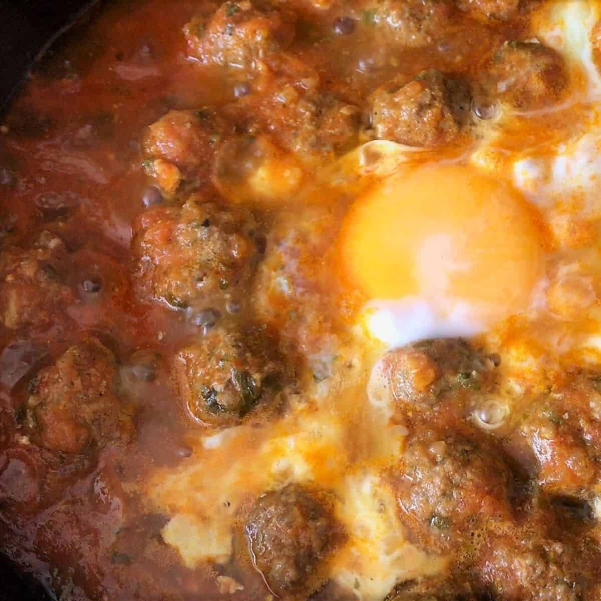 Savory meatballs cooking in tomato sauce with a runny egg on top, homemade pet friendly petitgourmet meal, delicious and nutritious, suitable for pet dogs and cats, high-quality ingredients, easy to prepare, perfect for healthy pet food recipes.