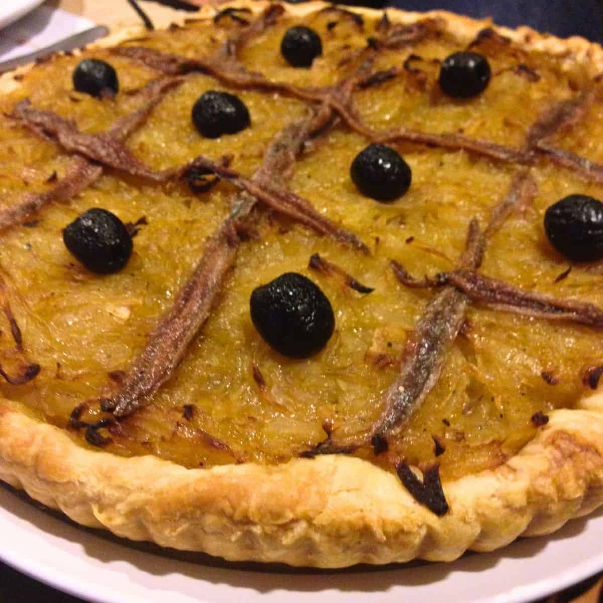 Crispy savory gourmet tart with black olives and anchovies, perfect for peti gourmet catering and special occasions, gluten-free, delicious ingredients, handcrafted bakery item.