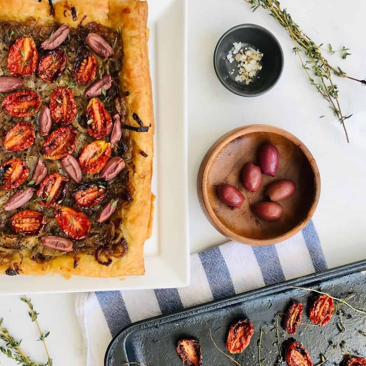 Fresh homemade tart with roasted cherry tomatoes, red onions, and herbs on a white platter. Perfect for gourmet snacks or light meals, highlighting artisanal ingredients and culinary craftsmanship.