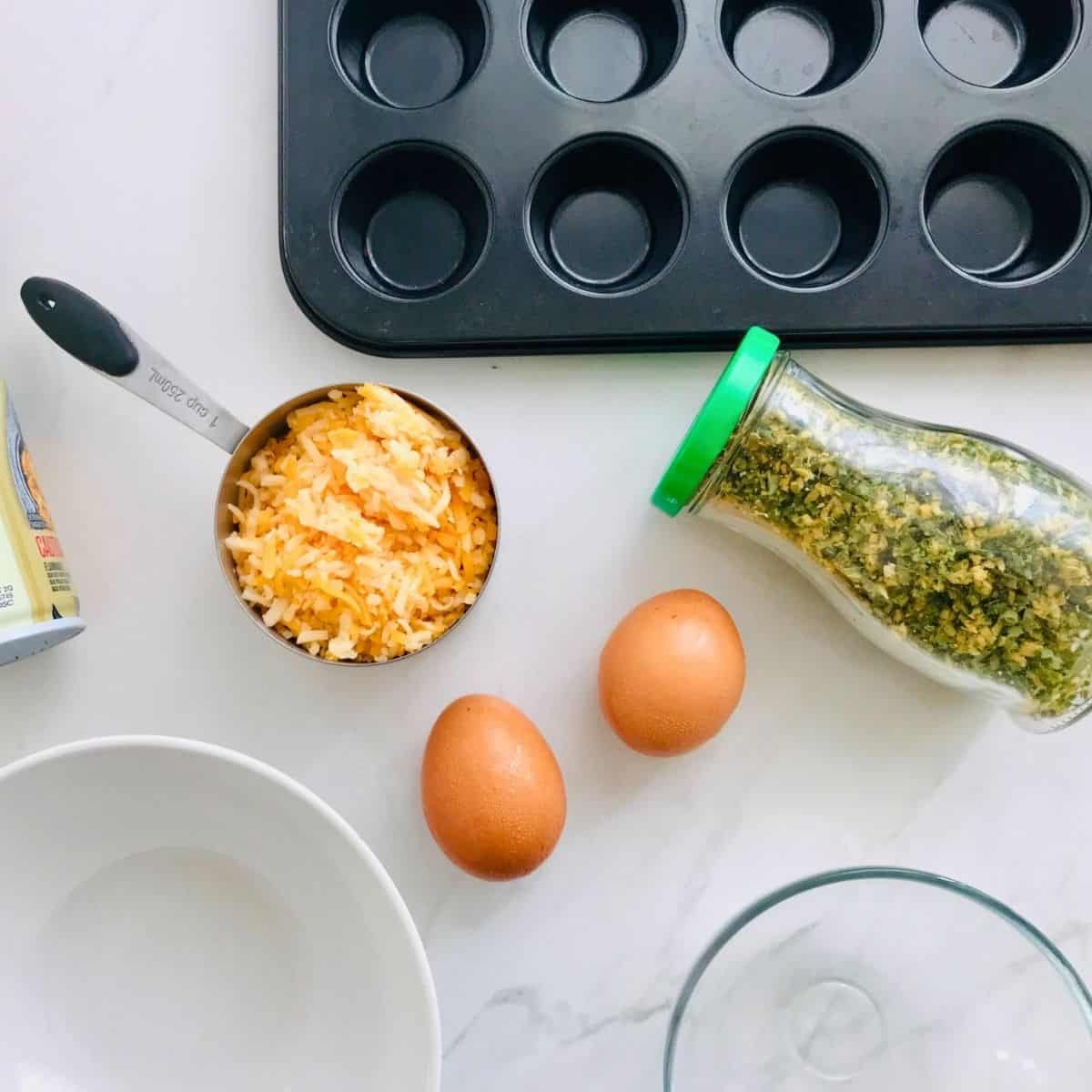 Cream-colored shredded cheese in a stainless steel measuring cup with a black handle on a white countertop.