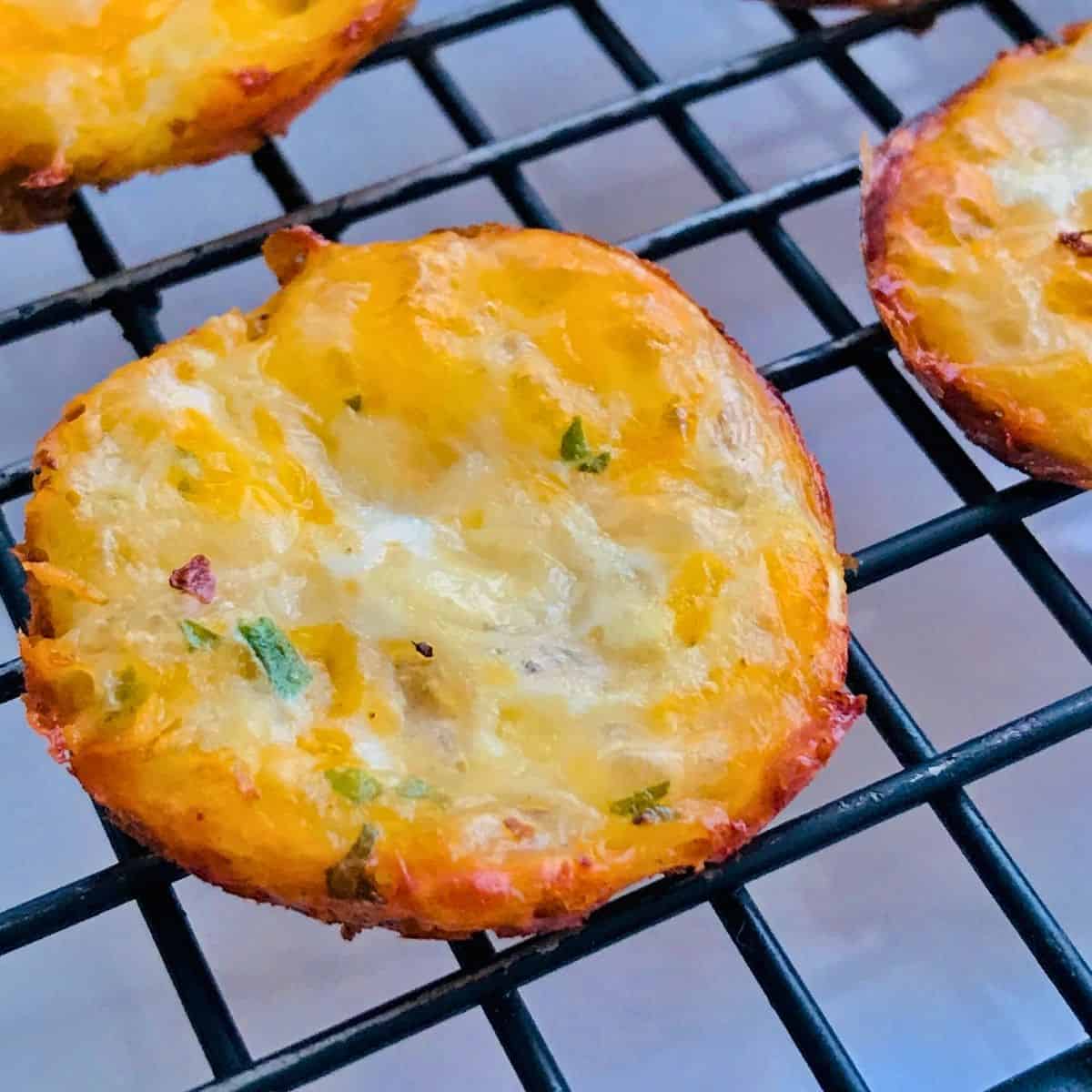 Crispy cheesy mini potato skins topped with melted cheese and herbs, served on a black grill rack, perfect appetizer for gourmet petiti dining experiences.