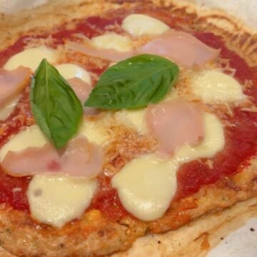 High-protein chicken crust pizza sliced on parchment with fresh basil