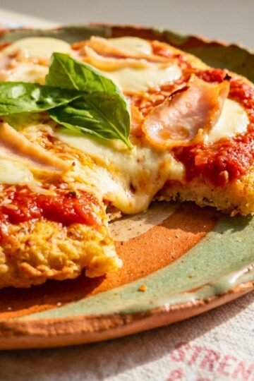 High-protein chicken crust pizza sliced on parchment with fresh basil