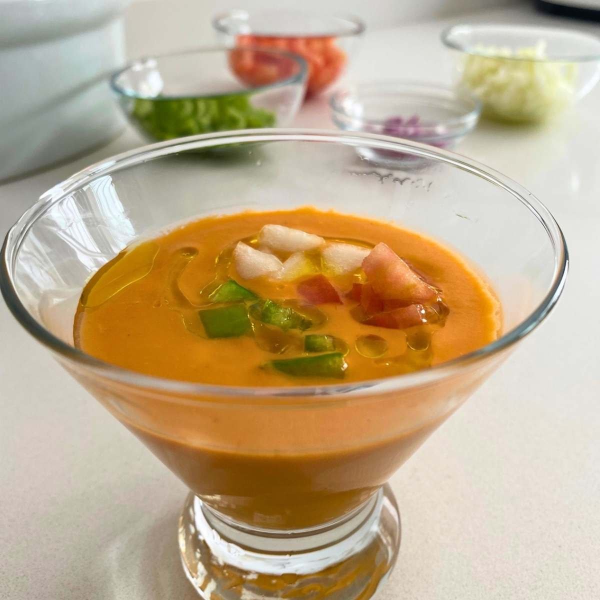 Gazpacho recipe: the 2-minute trick for a creamy, bread-free andalusian classic 7 overhead shot, gazpacho in a glass pitcher, ice cubes, bright red-orange color, garnished with diced cucumber