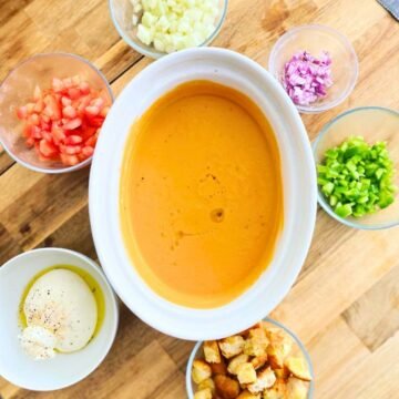 Gazpacho recipe: the 2-minute trick for a creamy, bread-free andalusian classic 4 overhead shot, gazpacho in a glass pitcher, ice cubes, bright red-orange color, garnished with diced cucumber
