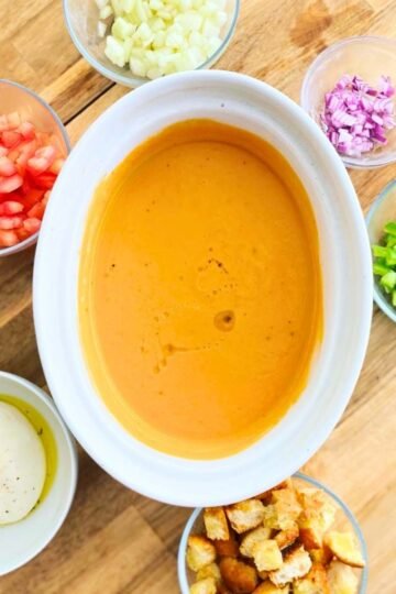 overhead shot, gazpacho in a glass pitcher, ice cubes, bright red-orange color, garnished with diced cucumber